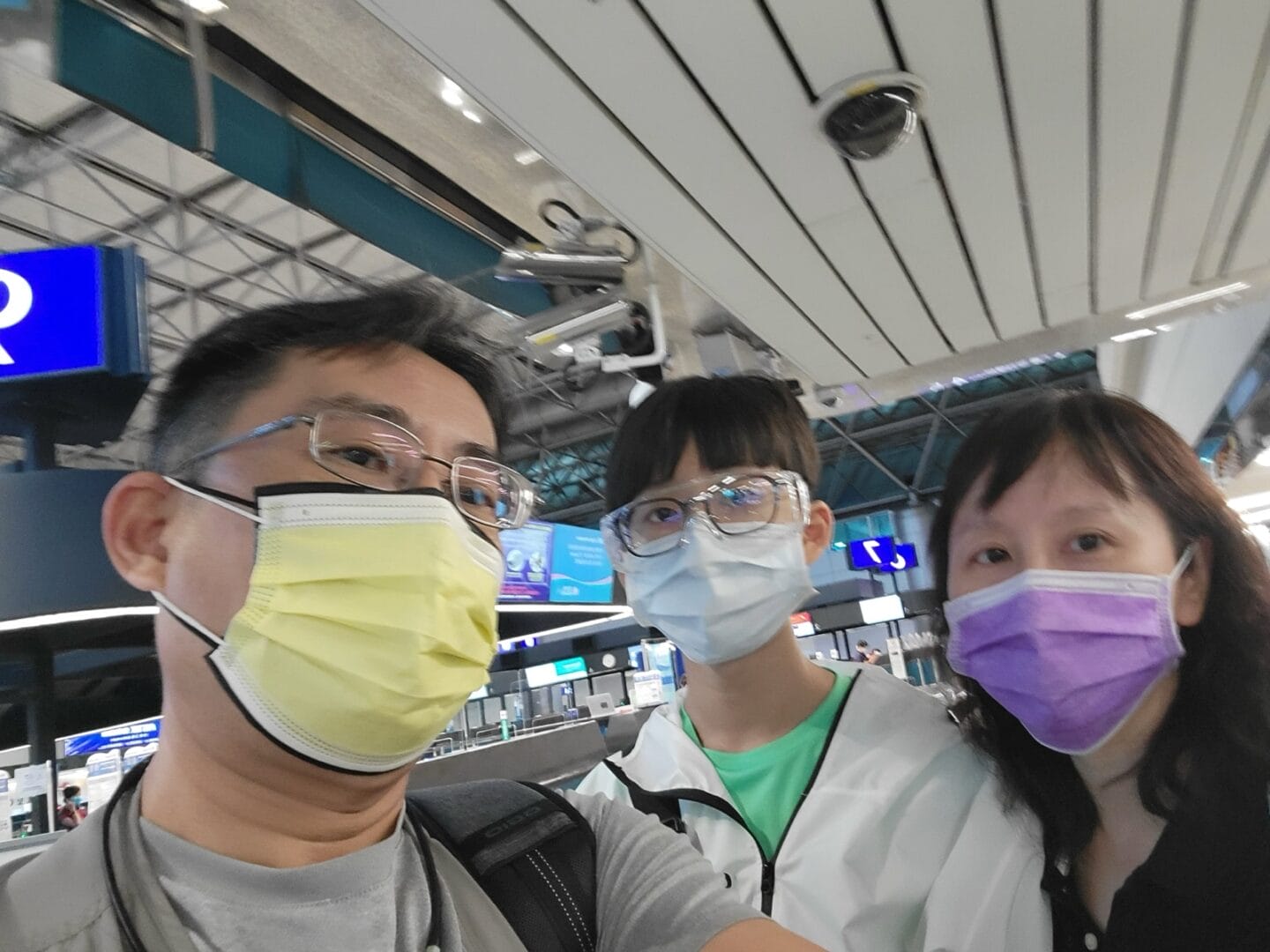 三名戴著口罩與眼鏡的人在機場航廈內自拍